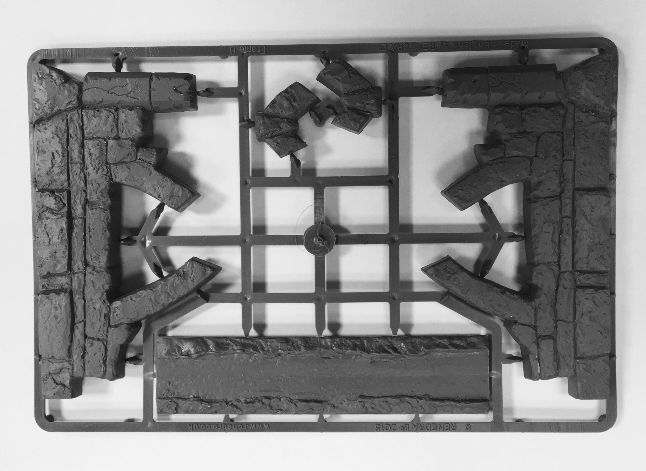 Unassembled gray hard plastic sprue frame from the Renedra Ruins Frame B scenery kit showing broken stone arch walls rubble blocks and base