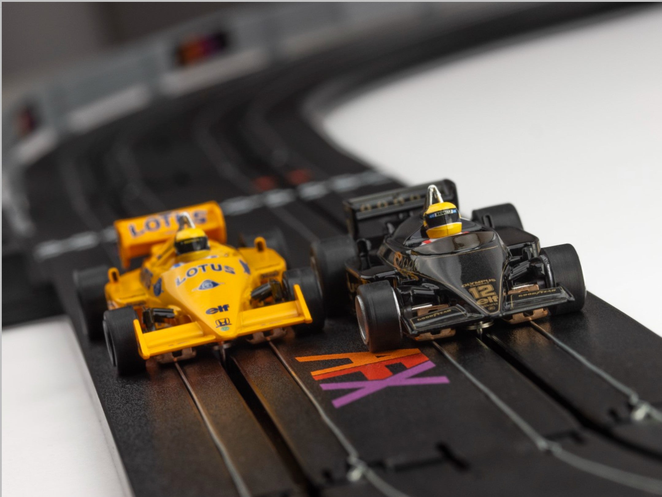Black Lotus 97T and Yellow Lotus 99T slot cars racing side-by-side on an AFX track layout.