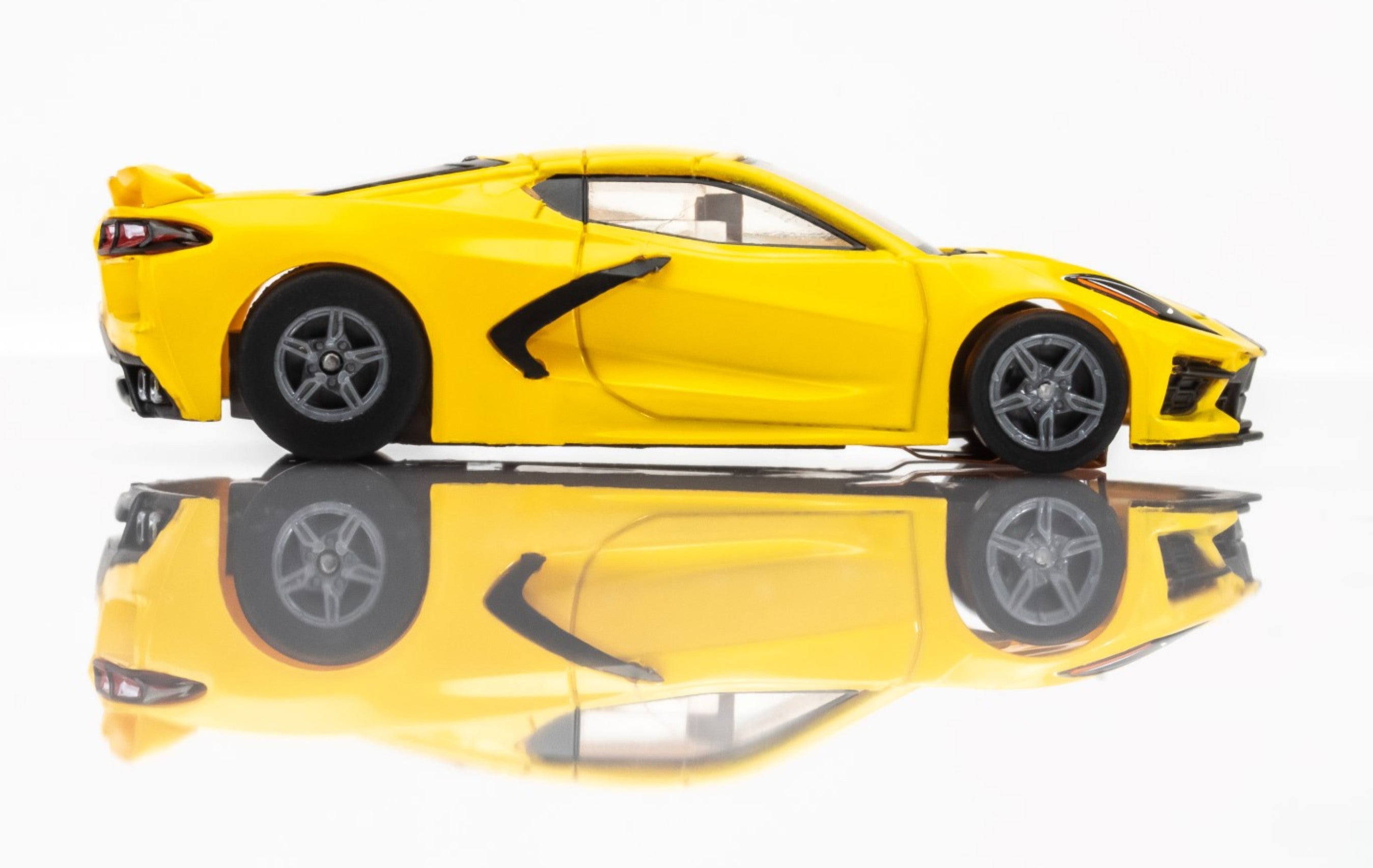 Side profile of AFX HO Corvette C8 slot car in yellow with silver wheels and racing stripes