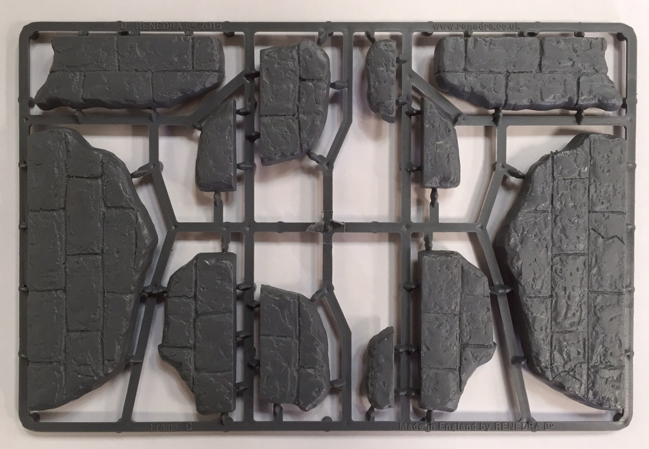 Unassembled gray hard plastic sprue frame from the Renedra Ruins Frame C scenery kit showing modular stone ruin walls and rubble components.