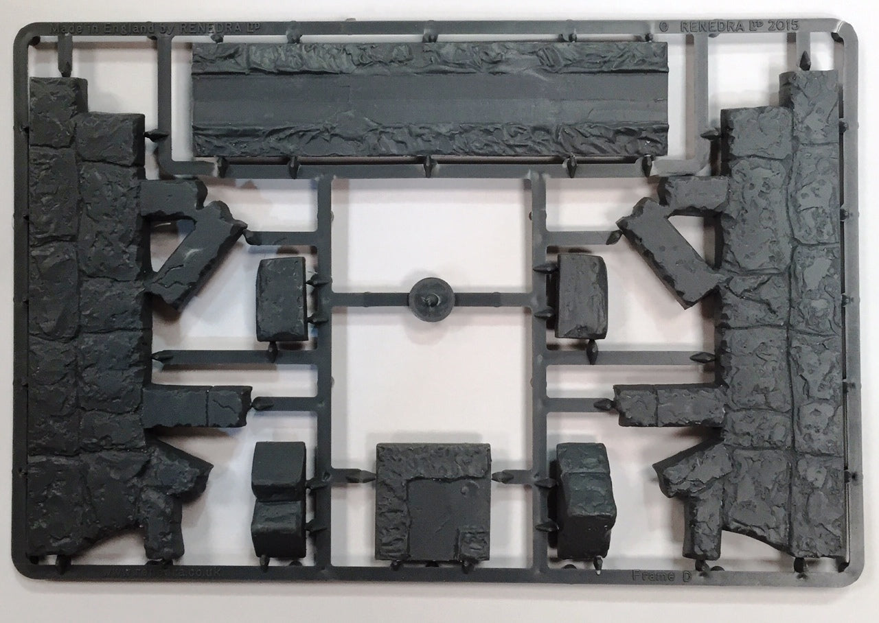 Unassembled gray hard plastic sprue frame from the Renedra Ruins Frame D scenery kit showing jagged stone corner walls rubble blocks and base