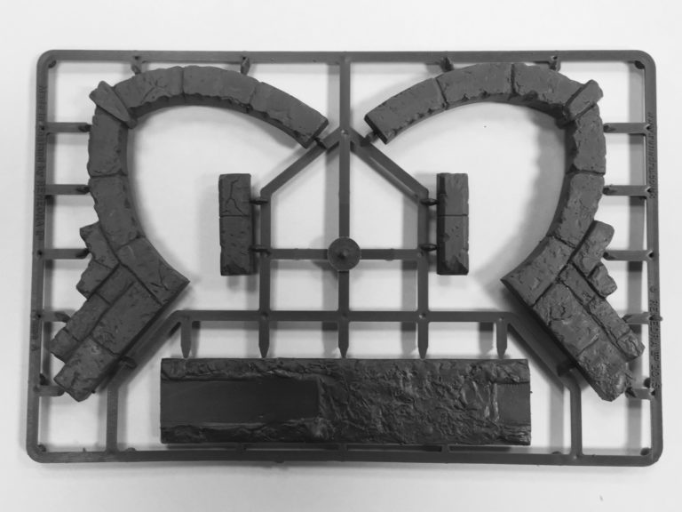 Unassembled gray hard plastic sprue frame from the Renedra Ruins Frame A scenery kit showing stone arch sections pillars and a base piece