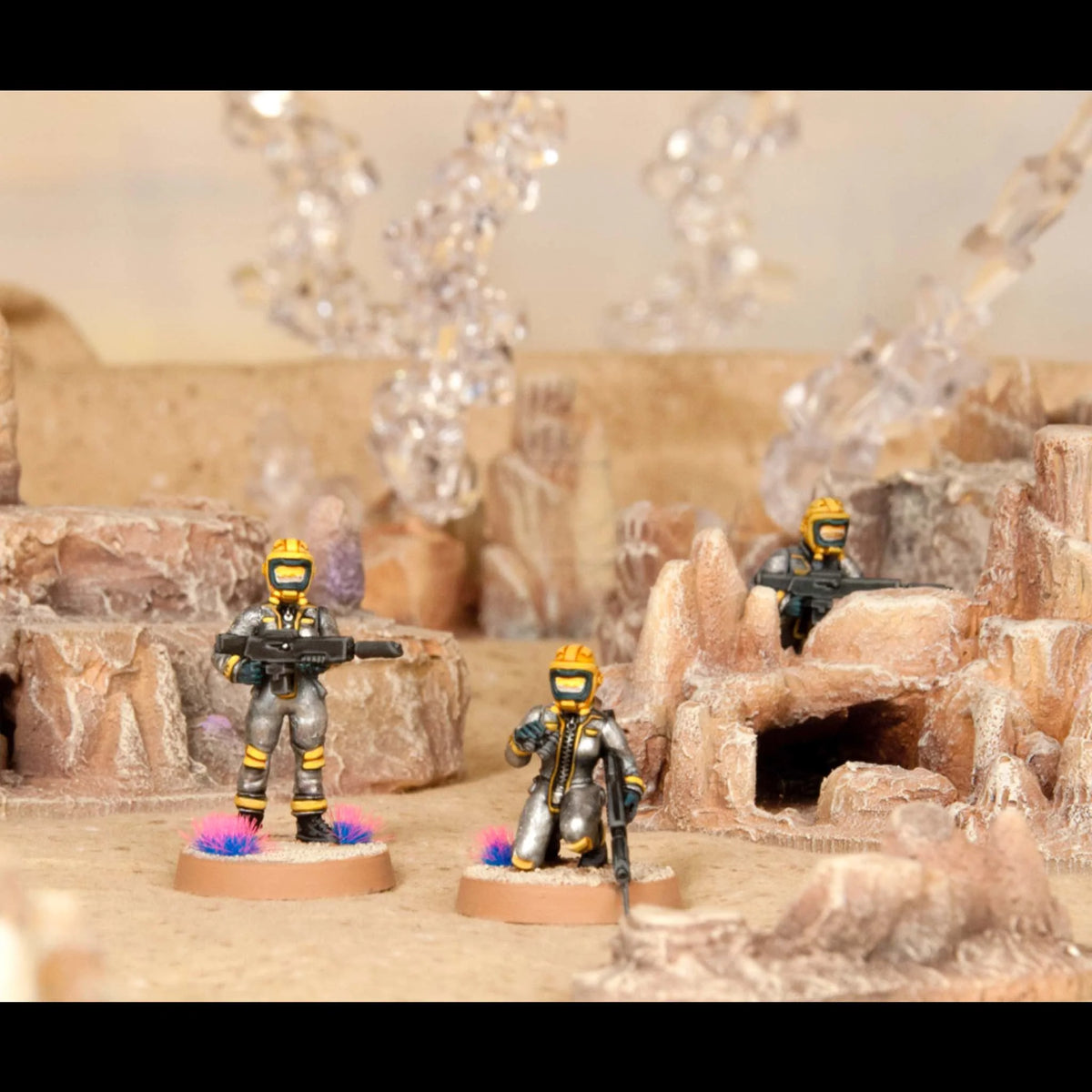 Three painted Cannon Fodder female miniatures in silver and yellow spacesuits on an alien terrain base