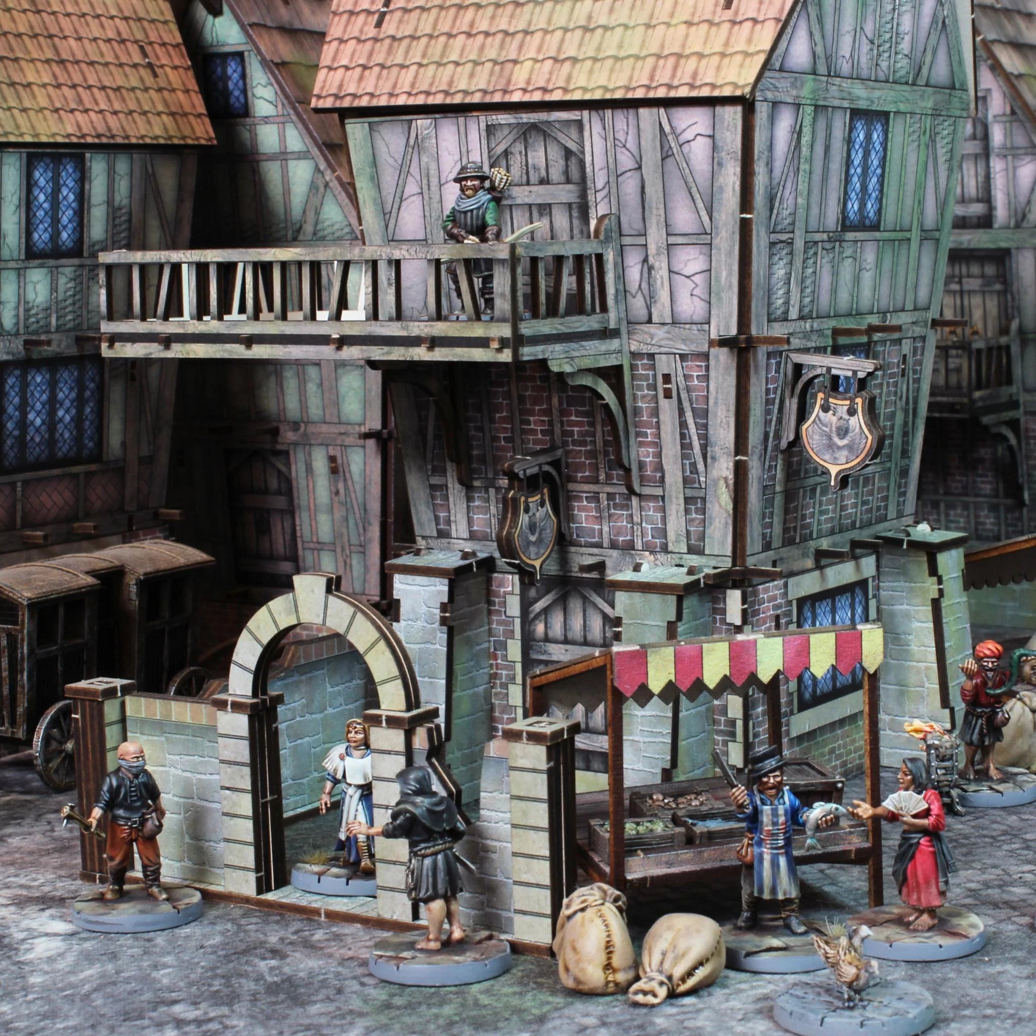 Assembled and painted fantasy villager miniatures standing outside medieval buildings and market stalls scene 2
