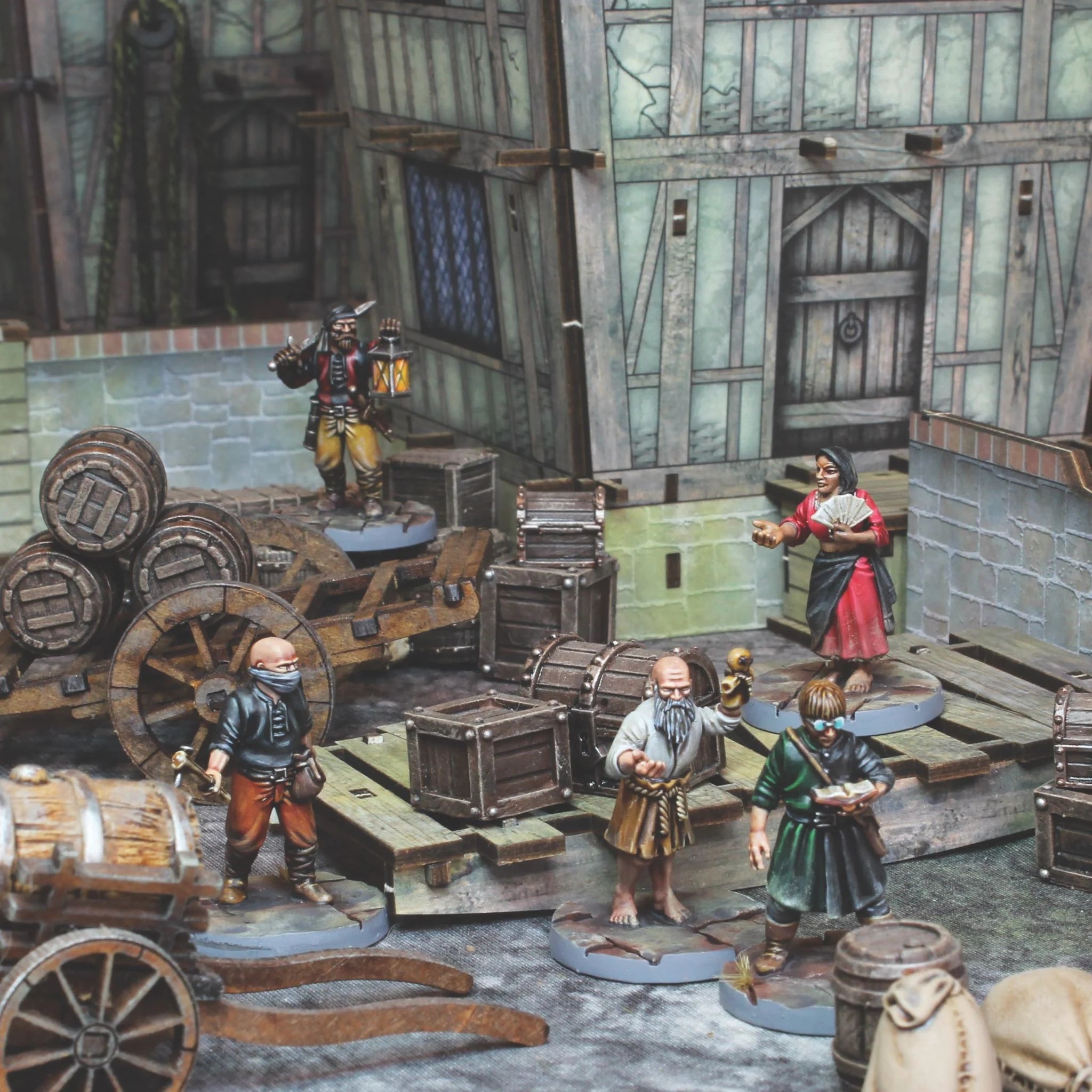 Painted civilian miniatures interacting around wooden crates and horse carts in a medieval town layout