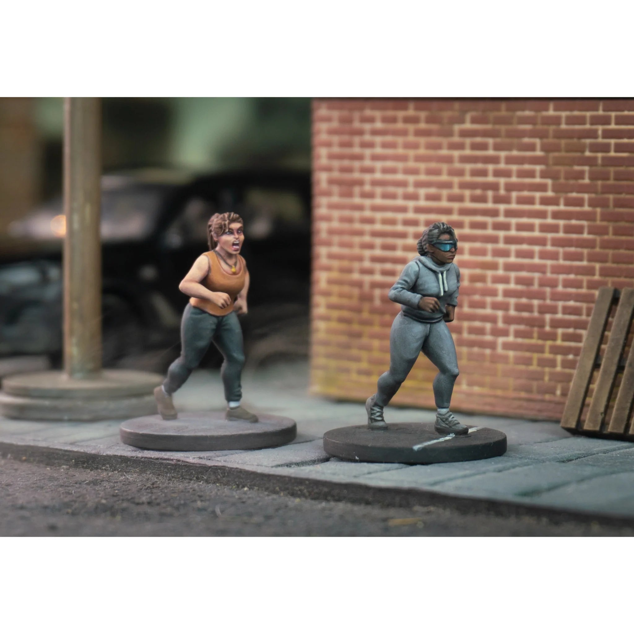 Two painted survivor miniatures running on an urban street in athletic wear and a gray hoodie