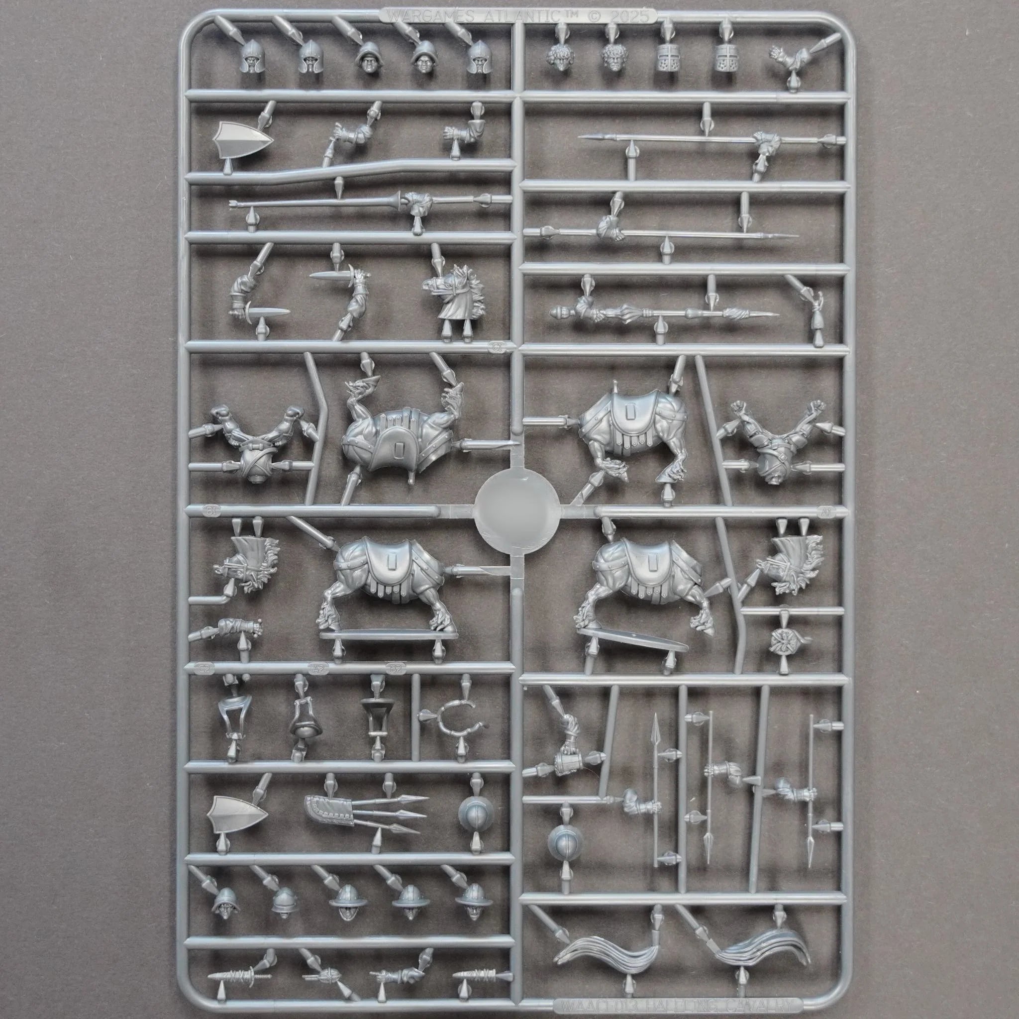 Front view of the unpainted gray plastic halfling cavalry sprue containing horse halves and weapon arms