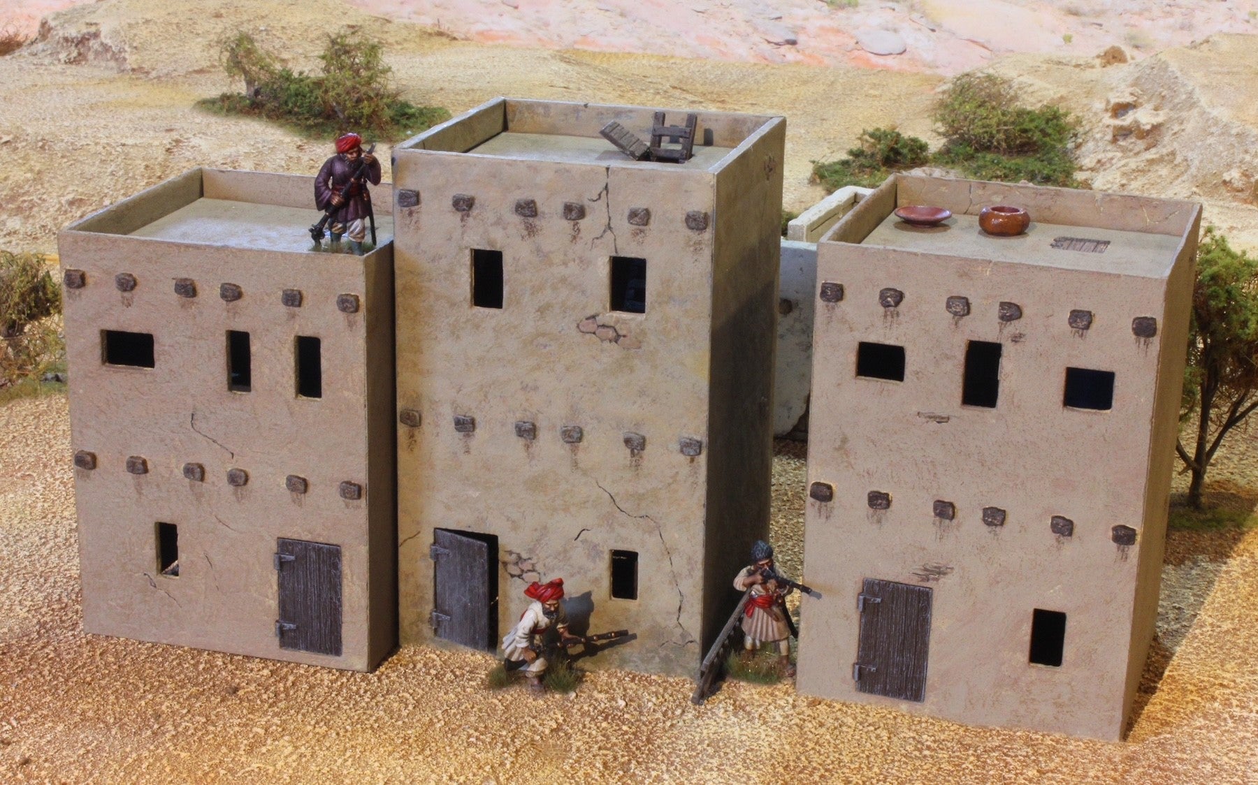 Three assembled and painted Renedra 28mm scale two-story adobe houses positioned together in a desert wargaming diorama.
